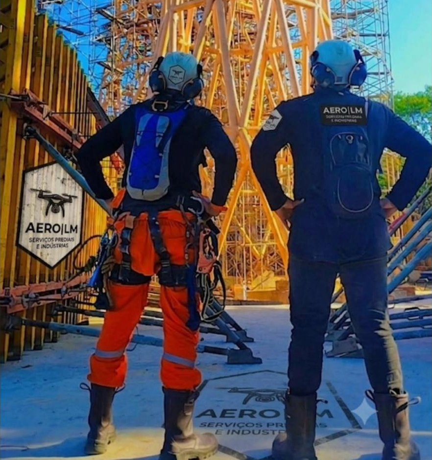 Dois técnicos da Aero LM equipados para acesso por corda diante de uma torre metálica